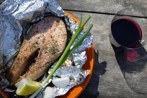 A trout cooked at the stake in orange plate on a wooden table outdoor. photo