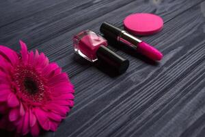 rosado productos cosméticos y gerbera flor en un oscuro azul de madera antecedentes. foto
