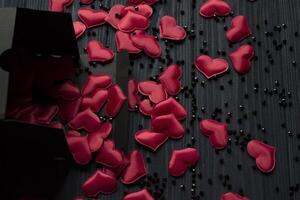 Red hearts are poured out of a black gift box on a dark blue wooden table. photo