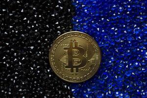 Golden bitcoin on a black and blue rhinestones. photo