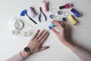 A woman painting her nails. Tools for manicure on a white wooden table. photo