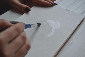 Woman paints in a sketchbook. Tools for painting on the white wooden desk. Painter work. photo