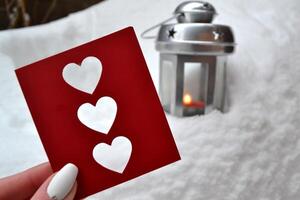 Red love card in female hand. Candle lantern on the snowdrift. Cold season. Hygge style. photo