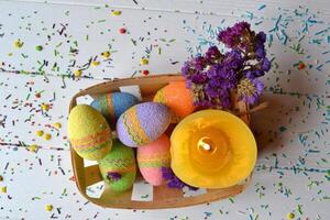 vistoso Pascua de Resurrección huevos con flores y amarillo vela en el cesta. hermosa Pascua de Resurrección antecedentes. Pascua de Resurrección tarjeta. hecho en casa fiesta decoración. foto