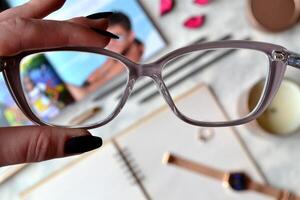 Eyeglasses in a female hand over a workplace with blur effect. photo