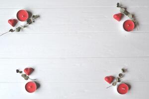 Red candies in a form of heart and red candles on the white wooden table. Background for greeting card on Valentine's day with place for text. photo