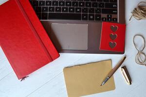 Red sketchbook, laptop, pen and empty sheet on the white wooden desk. Top view. Business workplace. photo