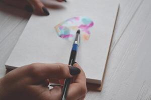 Woman paints in a sketchbook. Tools for painting on the white wooden desk. Painter work. photo