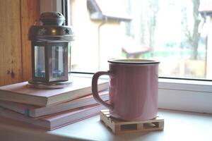 Books, candle lantern and a cup of tea on the window sill. Cozy living interior. photo