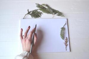 blanco papel con decoración en el blanco de madera escritorio, parte superior vista. el lápiz en mujer mano. foto