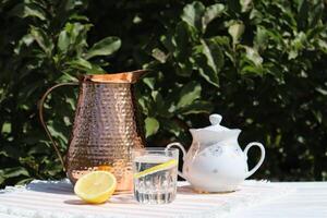 Copper pitcher and water with lemon on the wooden table outdoor. Summer still life with water and pitcher. photo