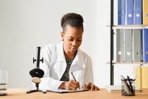 Scientific young woman looking at you while working at laboratory with a microscope. photo