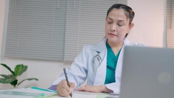 Foreign female doctor uses a laptop computer sitting at a table in the hospital health care and medical technology video