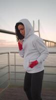 a woman in a hoodie and red gloves is practicing boxing on a bridge video