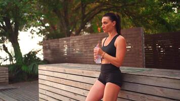 a woman in black shorts and a sports bra drinking water video