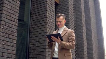 Handsome startup businessman using tablet. Young man texting messages, cheating on his tablet near the office. Business. Social networking video