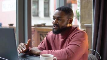 afrikansk amerikan ung man kommunicerar förbi konferens ring upp tala ser på dator i Kafé video