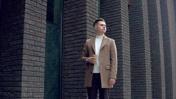 Handsome businessman in brown coat with coffee near the office looking at the camera video