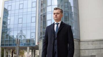 Stylish elegant male businessman in blue jacket and coat near office center looking at the camera video