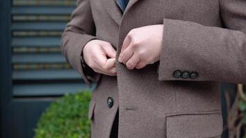 Close-up of a man buttoning his coat. Young elegant male businessman in brown jacket and coat near office center video