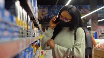 el niña en un máscara elige productos en el estantería en el supermercado video