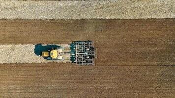 aérien Haut vue le terre dans le champ est étant cultivé en utilisant une tracteur cette a une charrue attaché à il video