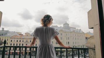 A woman in her hands on the balcony of a house looks happily at the city video