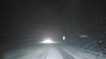 Nevado la carretera en coche faros a noche, vehículo faros iluminar un Nevado la carretera durante un tormenta de nieve a noche. video