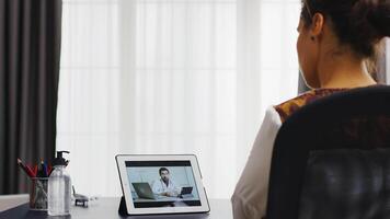 vrouw in een video telefoontje Aan tablet computer met haar dokter zittend Bij de kantoor.