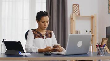 ennuyé femme navigation sur téléphone intelligent tandis que travail de Accueil bureau. video