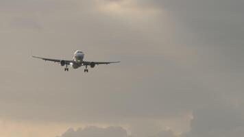 Footage of a jet plane approaching landing. Passenger airliner flies in the sunset sky, front view, long shot video