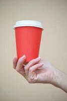 A woman's hand holds a paper red disposable cup for coffee. Mockup. Place for logo. photo