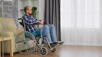 infeliz hombre en silla de ruedas en vivo habitación mirando a ventana. video