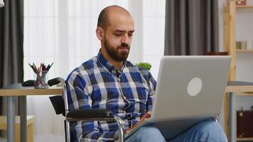 Handicapped freelancer in living room in wheelchair working on laptop . video