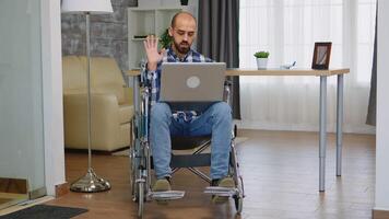 Businessman in wheelchair waving during a video call while working from home.