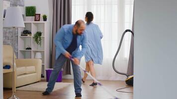 Mann wischen das Fußboden und das Ehefrau reinigt das Staub von Möbel. video
