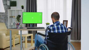 invalide homme dans fauteuil roulant travail sur ordinateur avec vert filtrer. video