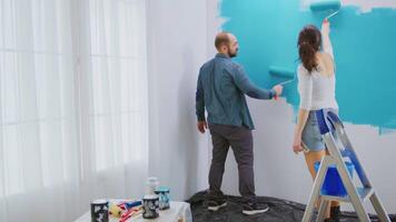 Caucasian couple painting wall with roller brush and blue paint. Apartment redecoration and home construction while renovating and improving. Repair and decorating. video