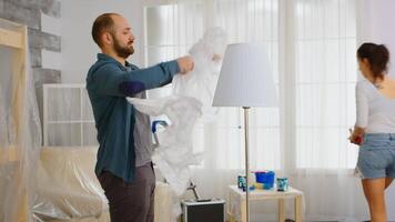 Man wrapping lamp with plastic foil before renovating living room. Married couple redecorating apartment. Construction, repair, home improvement, paint. video