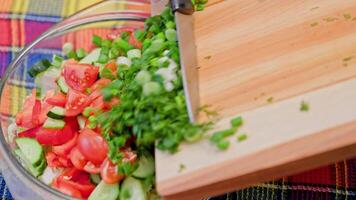 view of adding chopped green onion and dill into glass bowl with cut vegetables video