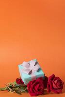 Valentine's day concept - gift box over bouquet of red roses on orange background. Copy space for your text photo