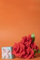 Valentines day concept - Bouquet of red roses and gift box on orange background. copy space for your text photo
