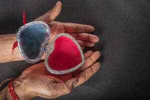 Female hands holding open heart shaped jewelry box on black background. photo