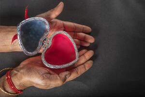 Female hands holding open heart shaped jewelry box on black background. Valentine's Day photo