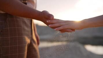 Sand through fingers close-up, against the backdrop of sunset. A guy and a girl pour sand out of their hands. The concept of lost time, life. photo