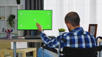 Man with disabilities sitting on wheelchair working on computer in his apartment. video