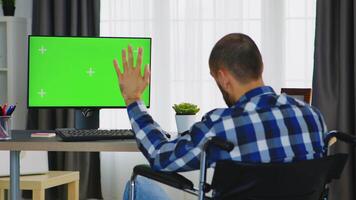 Invalid businessman waving during a video call on computer with green screen.