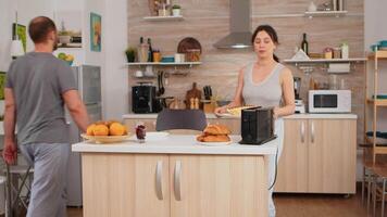 ama de casa en pijama preparando desayuno haciendo asado un pan en eléctrico tostadora. joven Pareja en el Mañana preparando comida juntos con afecto y amor video