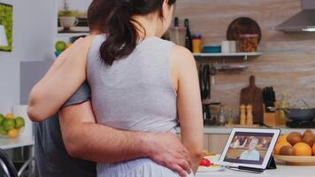 casado joven Pareja en vídeo llamada con madre durante desayuno en el cocina. joven Pareja en pijama utilizando Internet web en línea tecnología a charla con parientes y amigos video