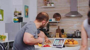 Entrepreneur on a video conference while eating breakfast in kitchen. Freelancer working remote, talking in videoconference video call online web internet meeting from home, communication device